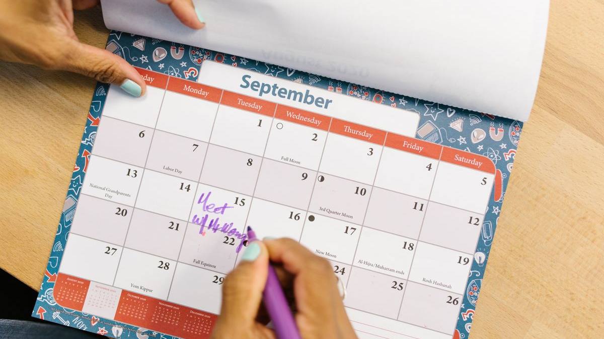 9月のカレンダーに紫のペンで予定を書き込む手元